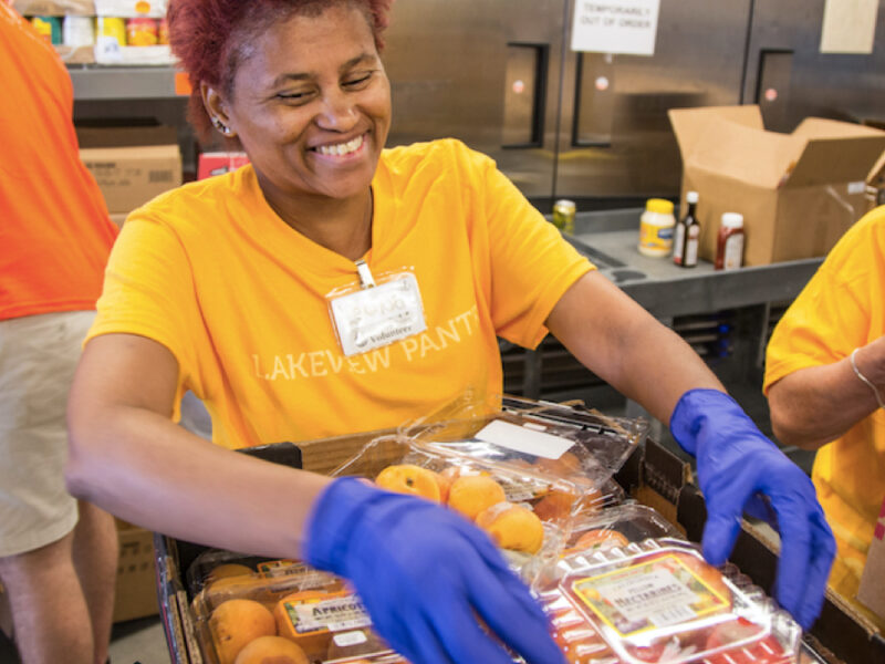 a woman at a food pantry holds a carton of tomatoes